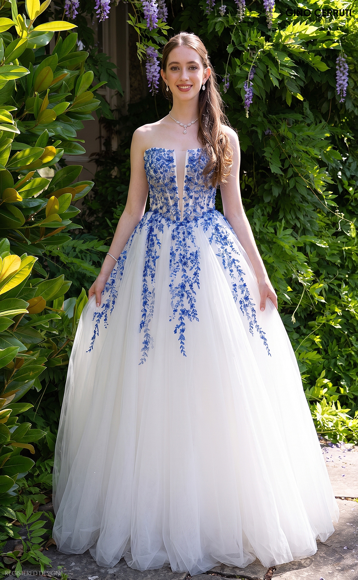 Model wearing an elegant ivory tulle ballgown by Gino Cerruti, featuring intricate royal blue floral embroidery, a strapless sweetheart bodice with a sheer plunge neckline and a flowing full skirt. A beautiful alternative wedding dress at MK Bride, Milton Keynes.